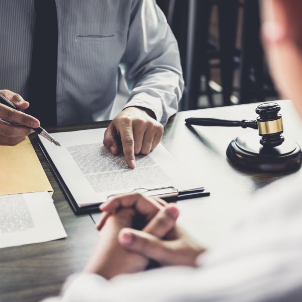 A person points at a document, guiding the seated client's attention, in a professional legal setting with a gavel on the desk indicating the context of law.
