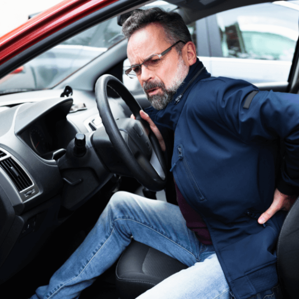 man in driver seat grabbing his back in pain