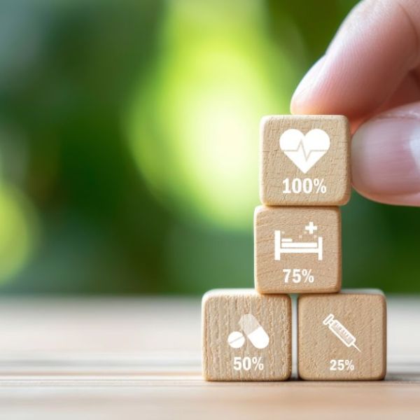 Wooden blocks displaying health-related percentages (100%, 75%, 50%, 25%) are arranged in a stack, with a hand poised to place the top block. The blurred green background suggests a natural setting.
