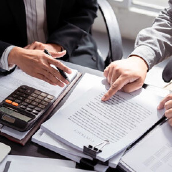 Two professionals reviewing documents and using a calculator for financial analysis at an office desk.