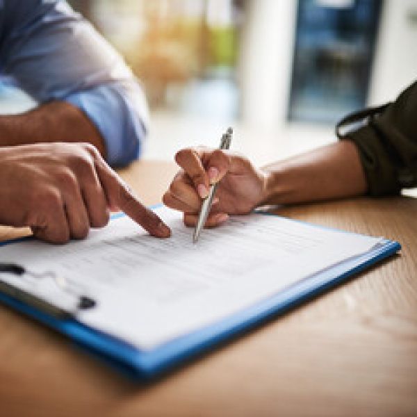 People reviewing and signing a document on clipboard, close-up of hands with pen and pointing finger.