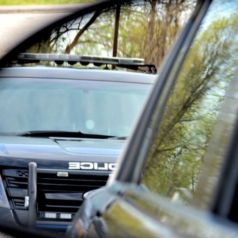 Police car reflected in side mirror on roadside, capturing a traffic stop scenario.