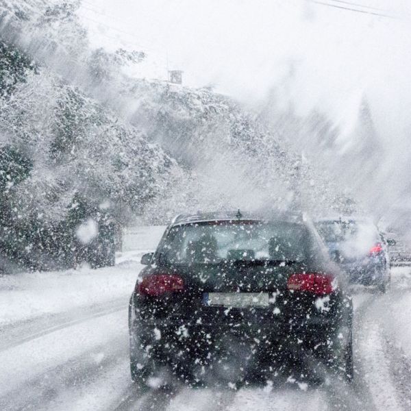 Cars driving cautiously in heavy snowfall on a snow-covered road.