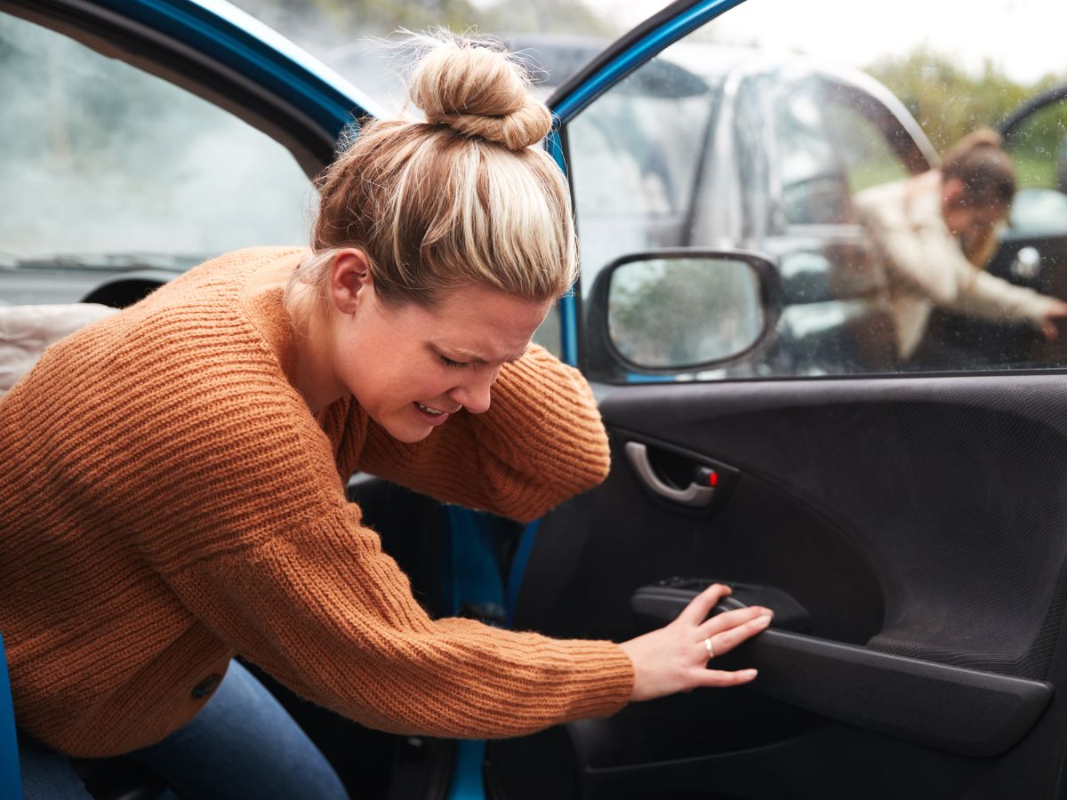 Woman getting out of car holding neck