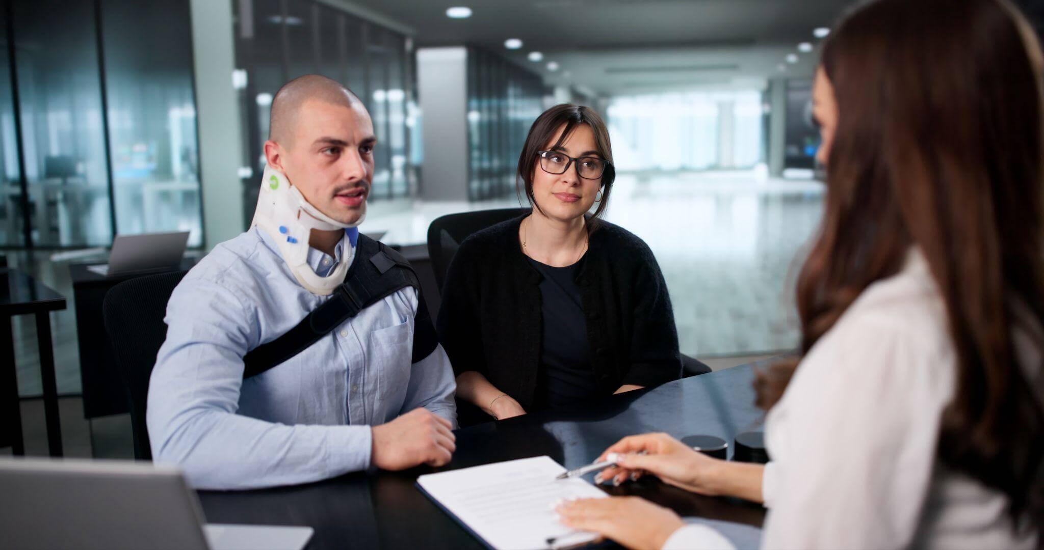 a woman and a man sitting at a table talking to a person representing a business, the man is wearing a neck brace