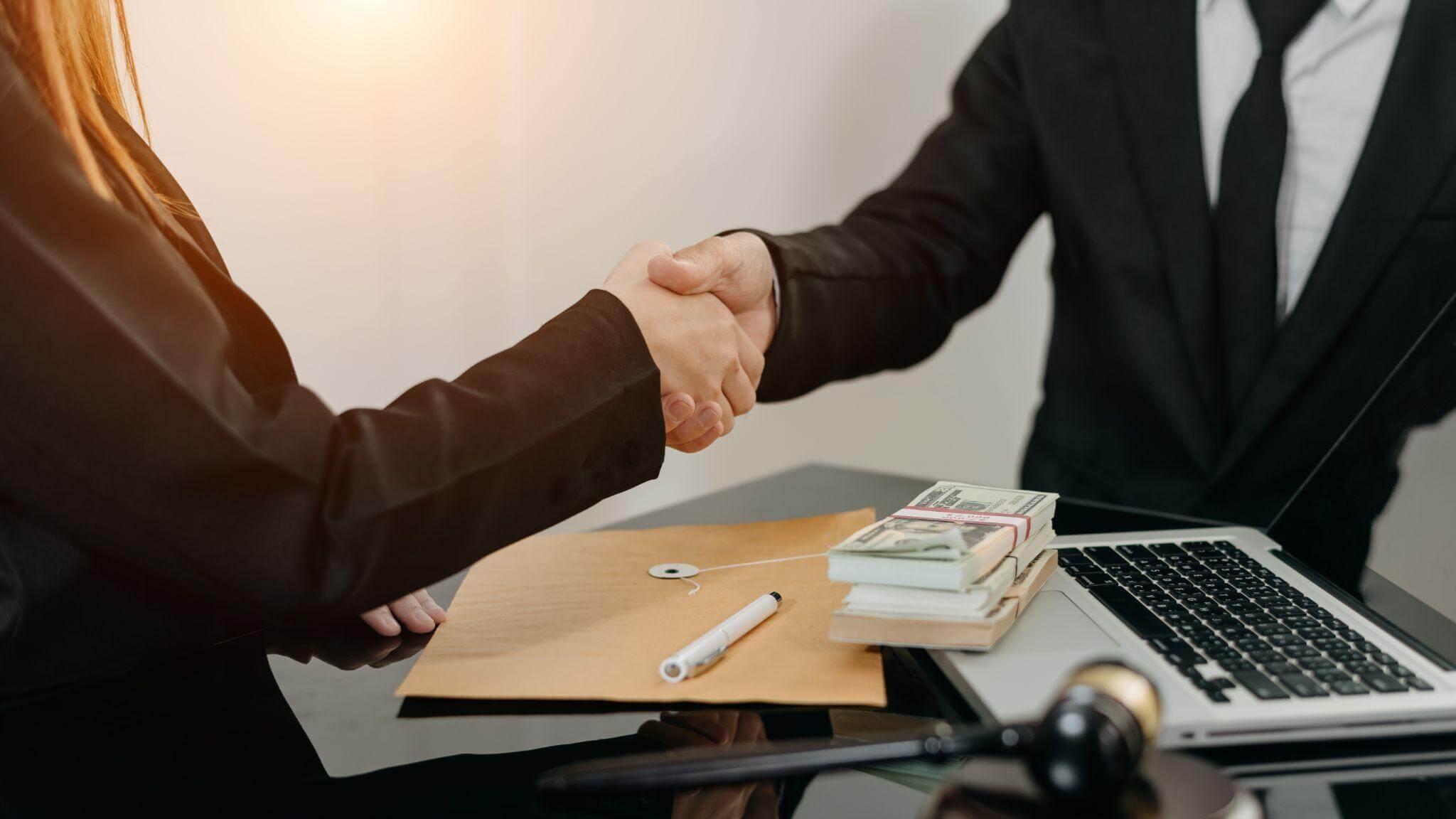 two people shaking hands in front of a laptop